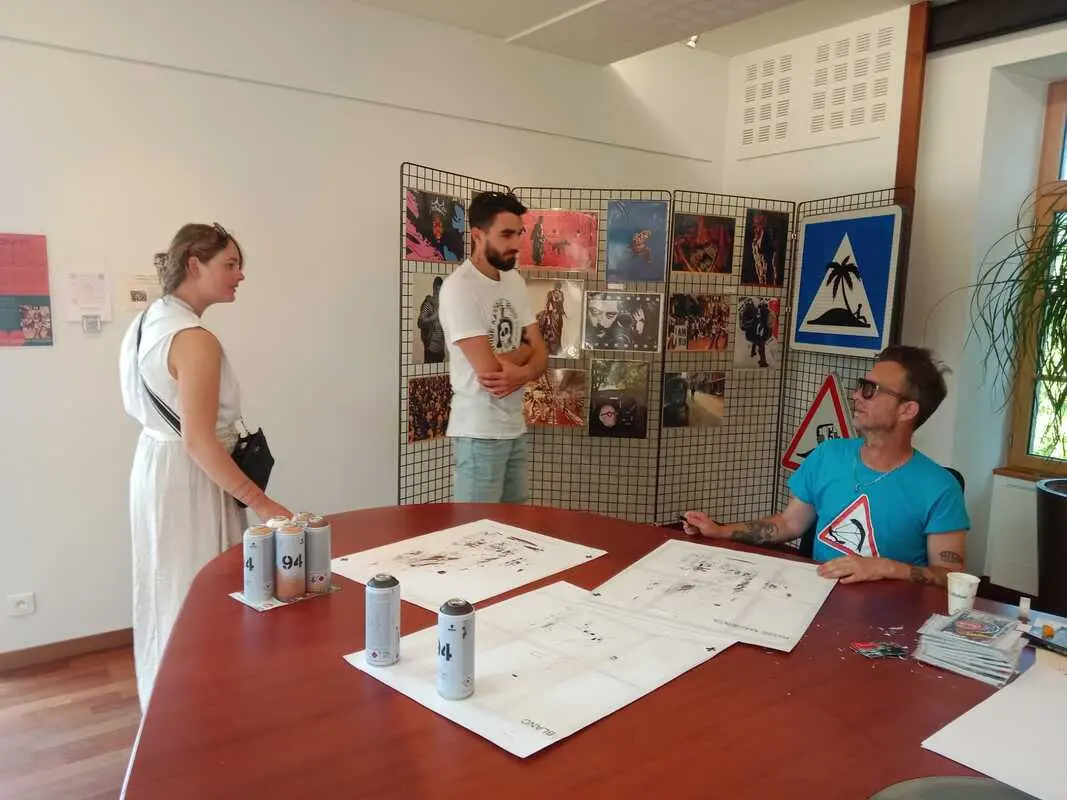 Artiste peintre et dessinateur assis à une table qui présente ses œuvres à un public composé de deux personnes