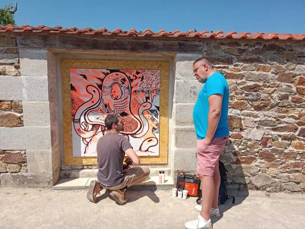 Fresque murale en extérieur realisée en direct par un peintre et un bénévole du festival est en train de discuter avec lui