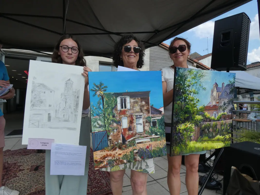Remise des prix des concours devant la mairie de Rocheservière où trois femmes artistes qui ont gagné un prix présentent leurs tableaux devant le public