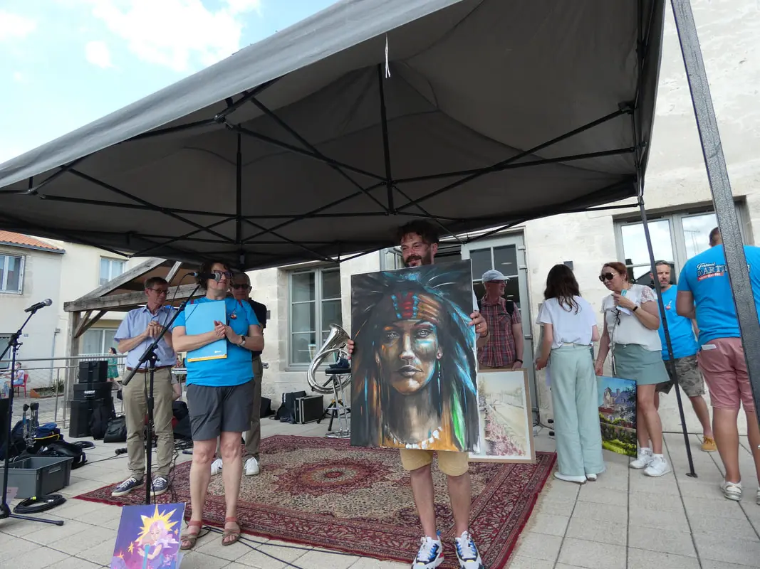Remise des prix des concours devant la mairie de Rocheservière en présence des bénévoles, du maire et d'un artiste qui a gagné un prix et montre son tableau au public