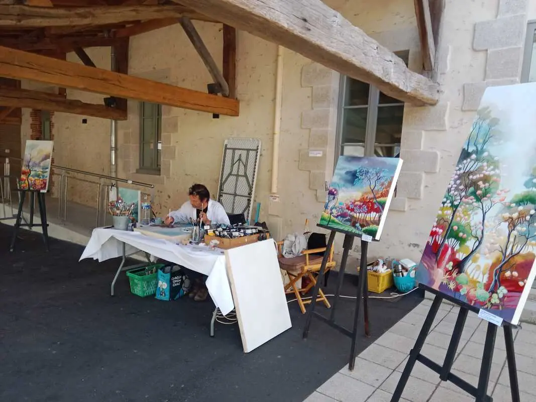 Peintre peingnant pendant le festival devant la mairie de Rocheservière et assi à une table